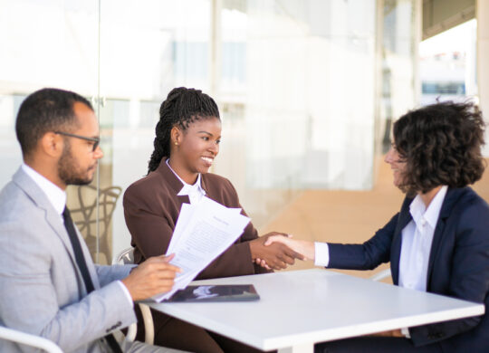 Business colleagues consulting legal advisor. Business man and women sitting at table outdoors and talking, man holding papers, women shaking hands. Consulting expert concept